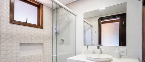 Un baño moderno con cabina de ducha de vidrio, un lavabo blanco y un espejo grande.
