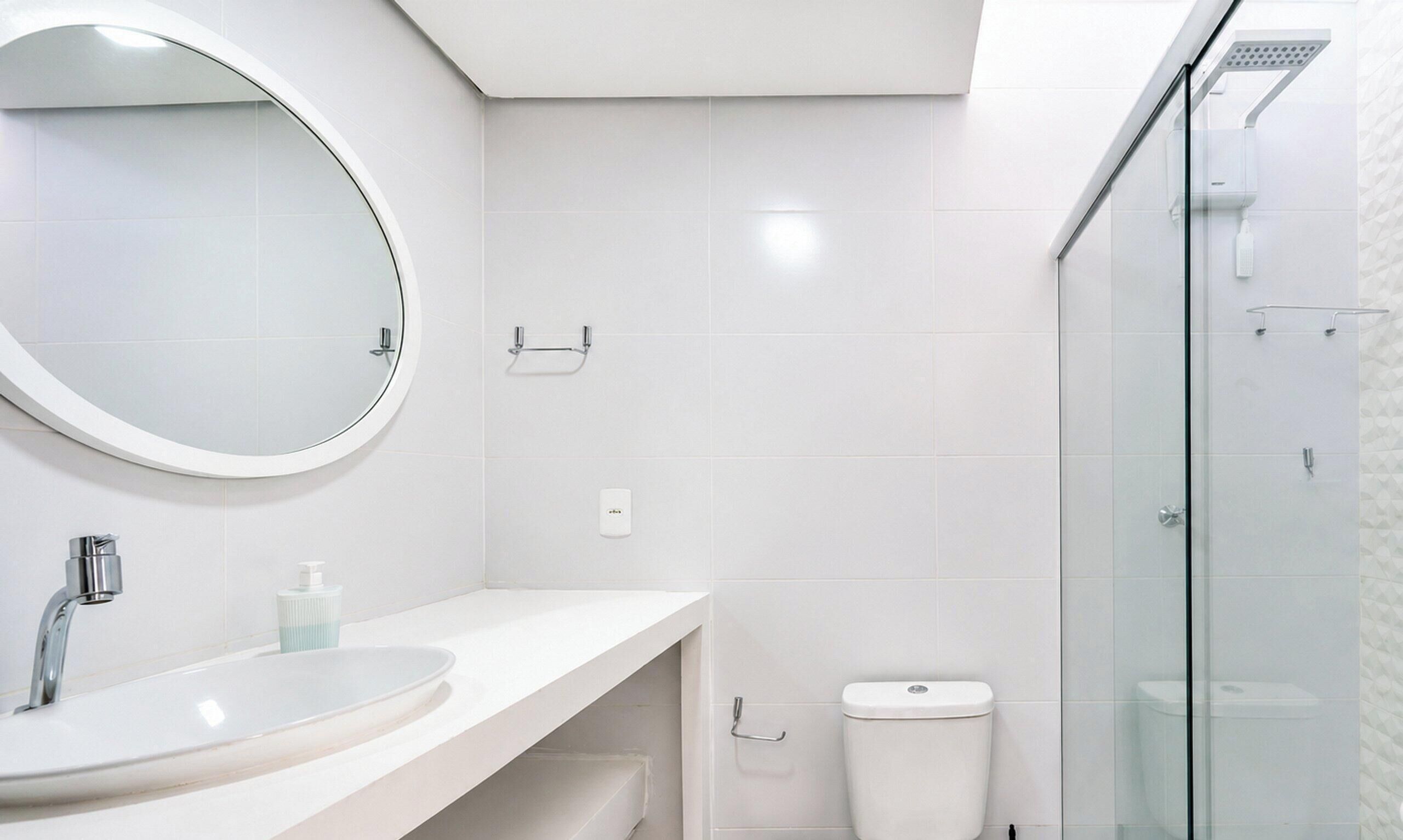 A modern bathroom with a round mirror, a sink, a toilet, and a glass shower enclosure.