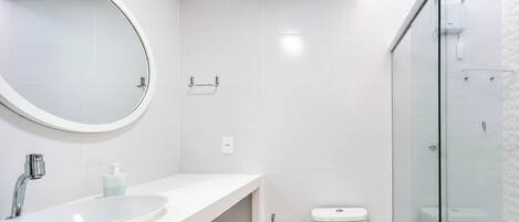 A modern bathroom with a round mirror, a sink, a toilet, and a glass shower enclosure.