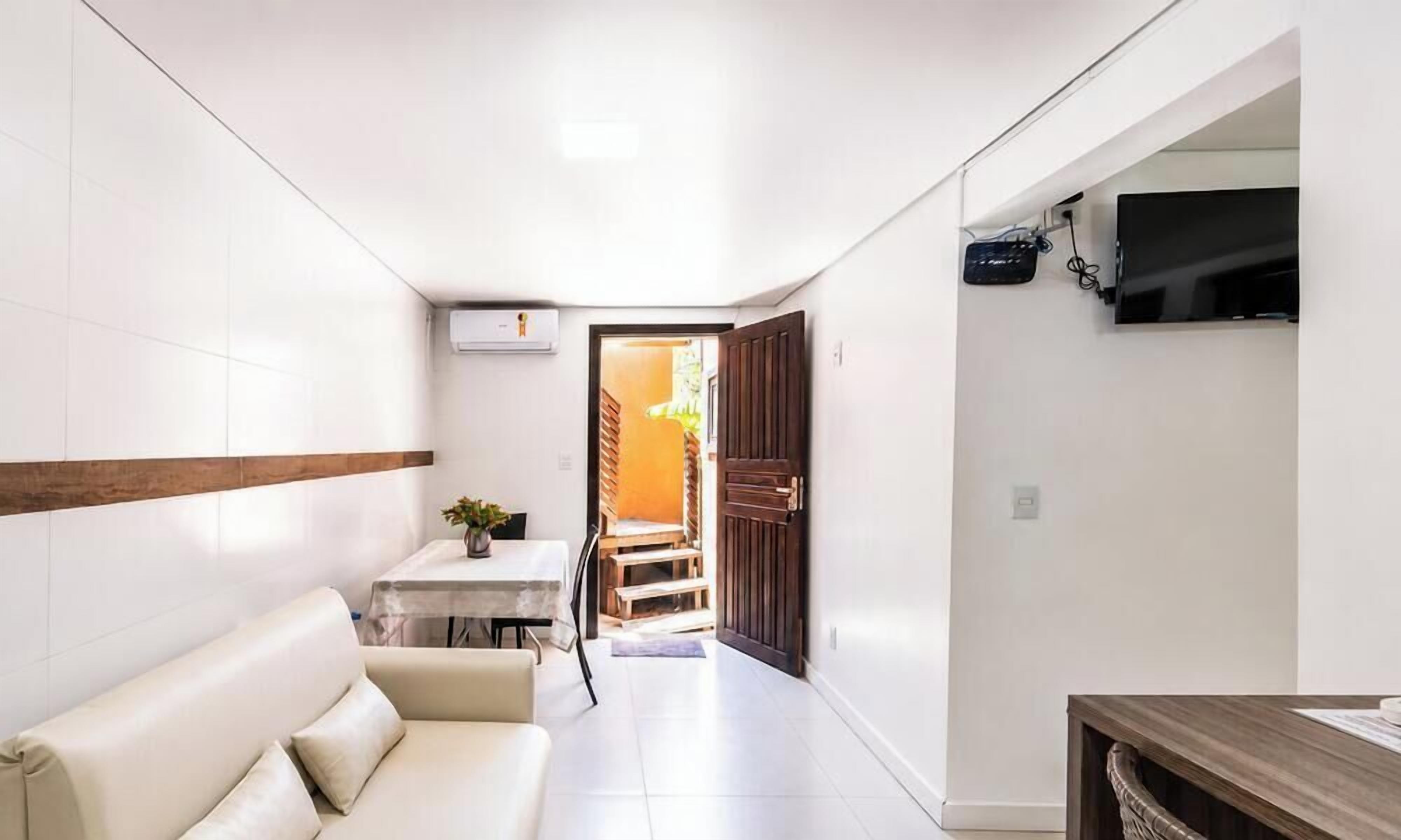 A narrow hallway with a white sofa, a small table with a plant, and a TV mounted on the wall.