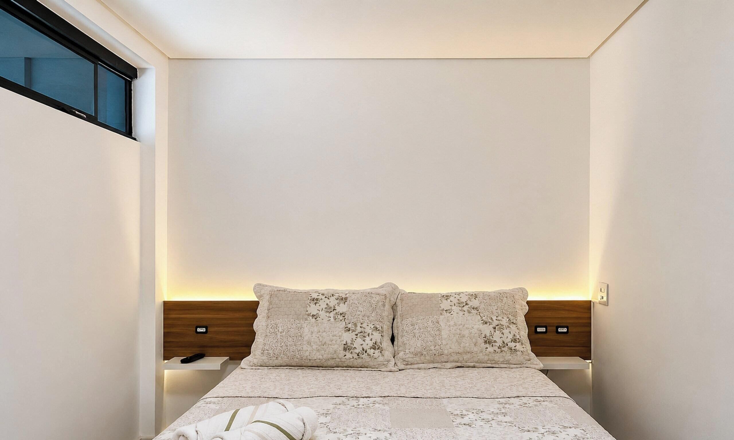 Une chambre à coucher comprenant un lit, deux oreillers, une table de chevet et une lampe fixée au mur.