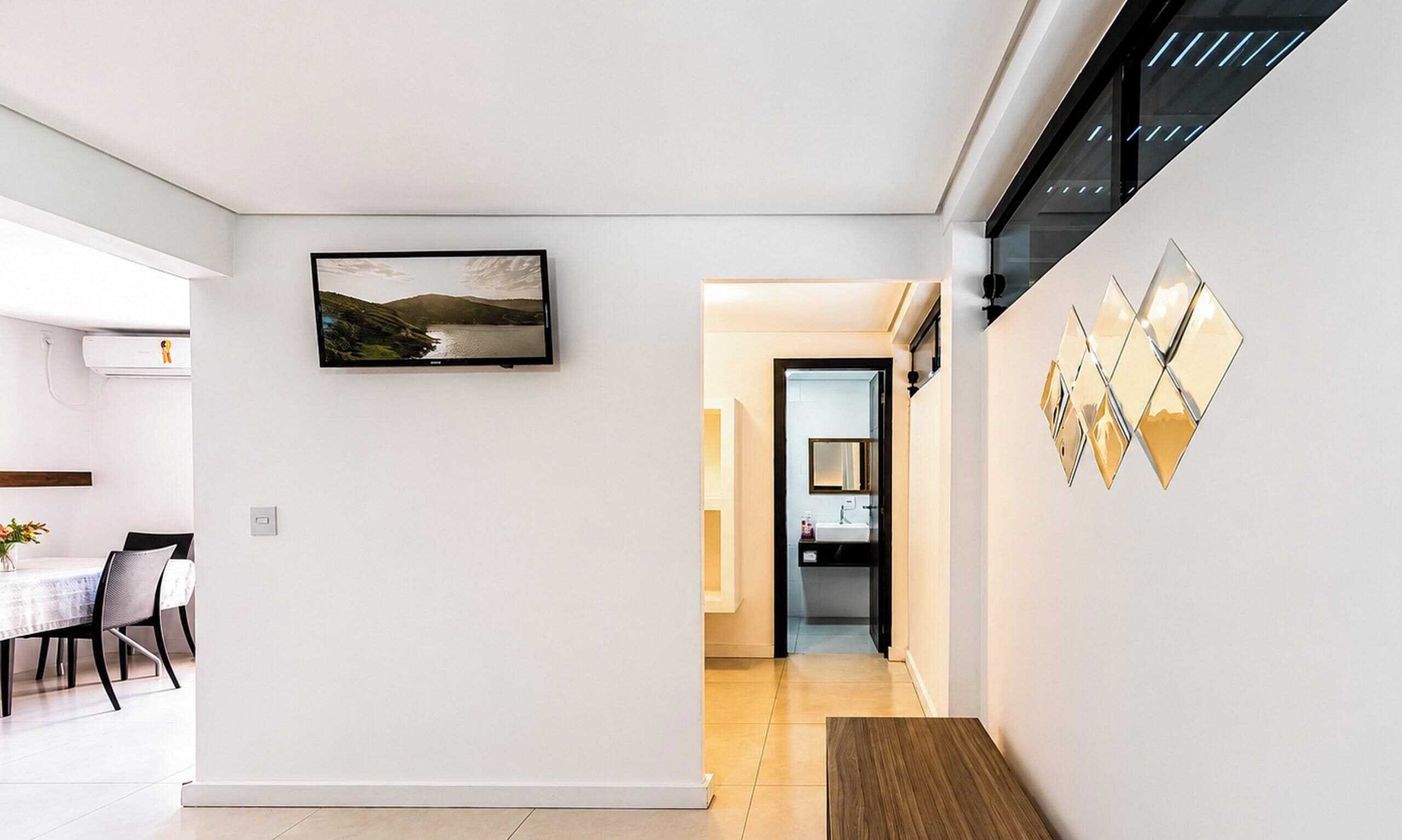 A modern interior with a dining area, a hallway leading to a kitchen, and a wall with a framed landscape photo and diamond-shaped mirrors.