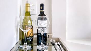 A minibar with two wine bottles and two glasses, a power outlet, and a set of cutlery on a tray.
