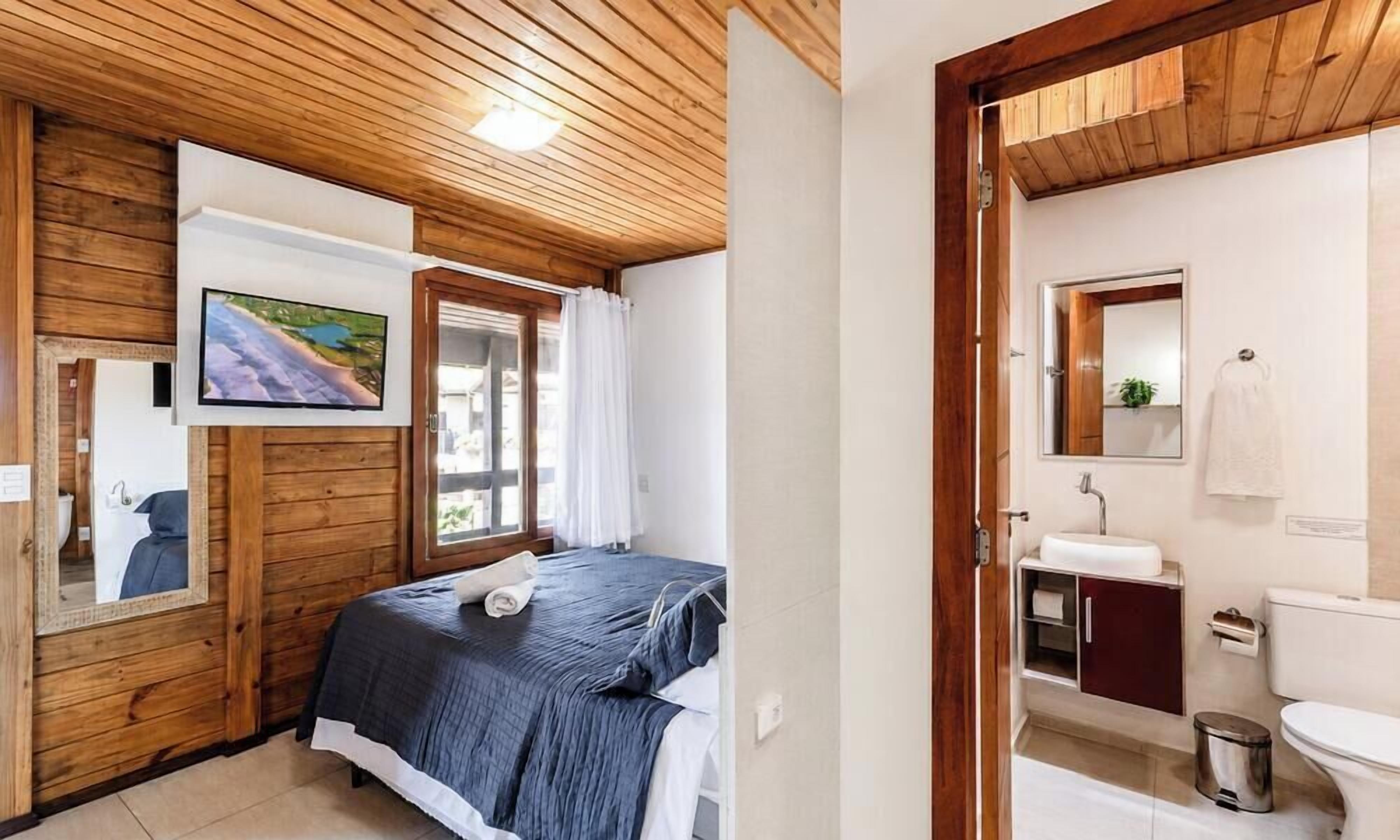 Une chambre à coucher comprenant un lit, un téléviseur, un plafond en bois, ainsi qu’une salle de bain avec des toilettes, un lavabo et un miroir.