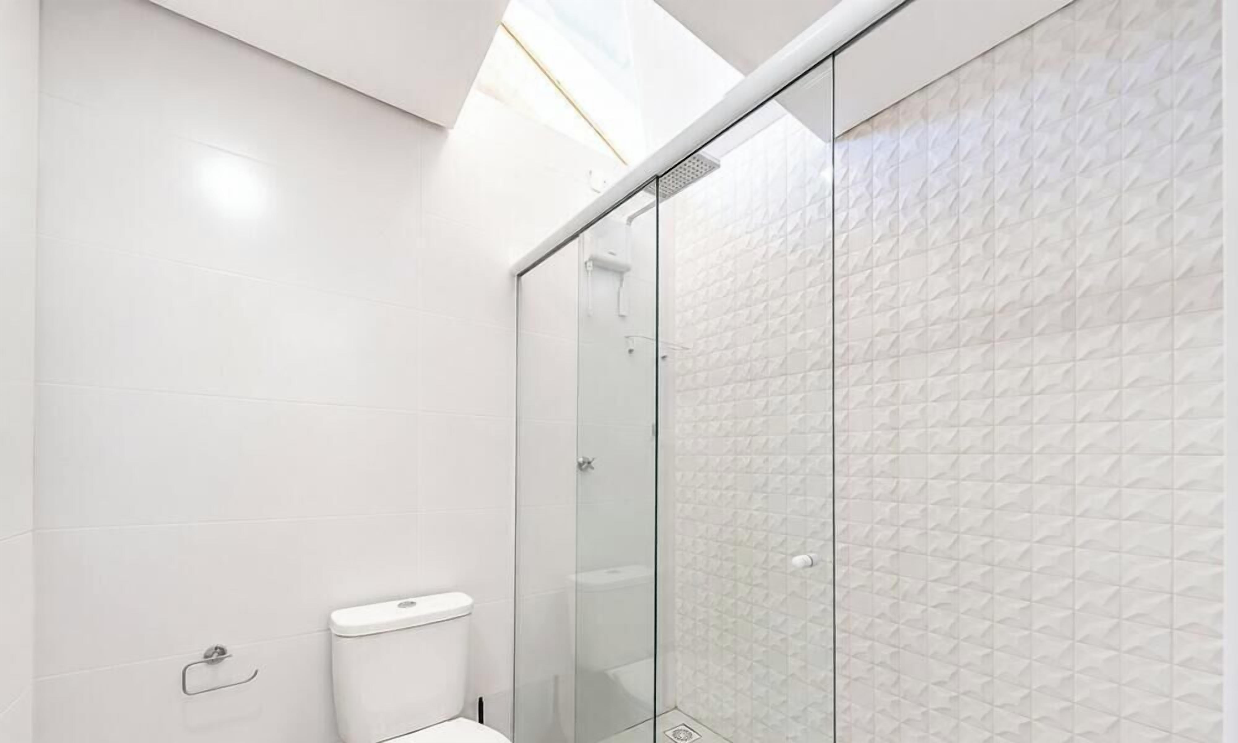 A modern bathroom with white tiles, a glass shower enclosure, and a skylight.