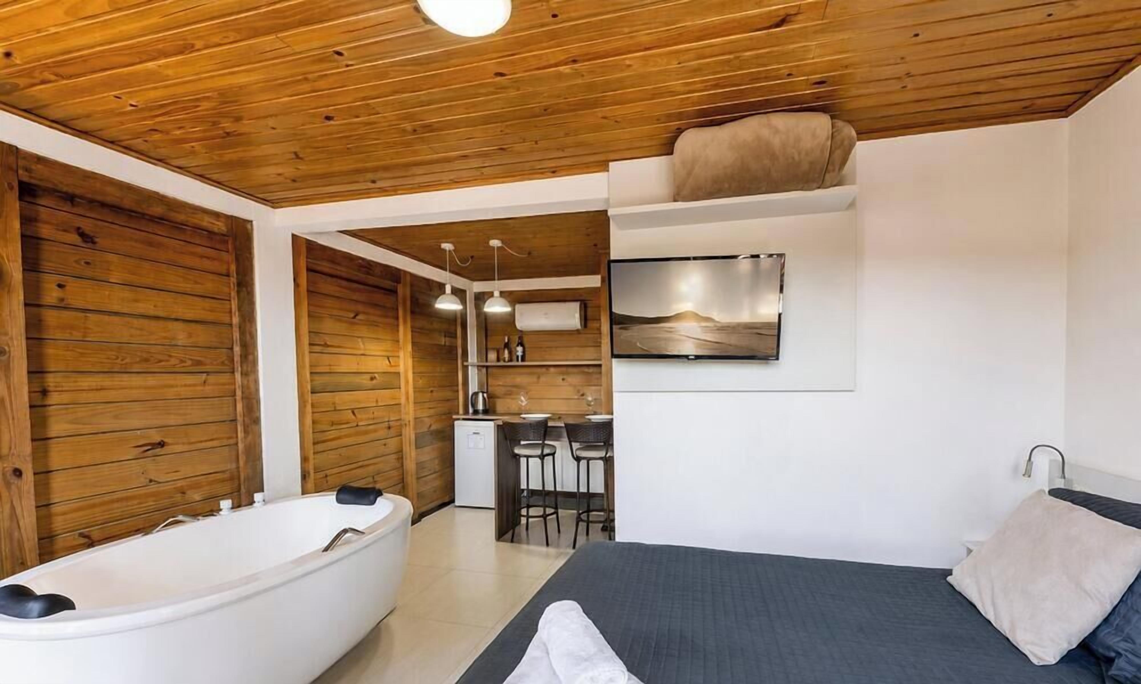 A room with a wooden ceiling, a bathtub, a bed, a small kitchenette, and a mounted artwork.
