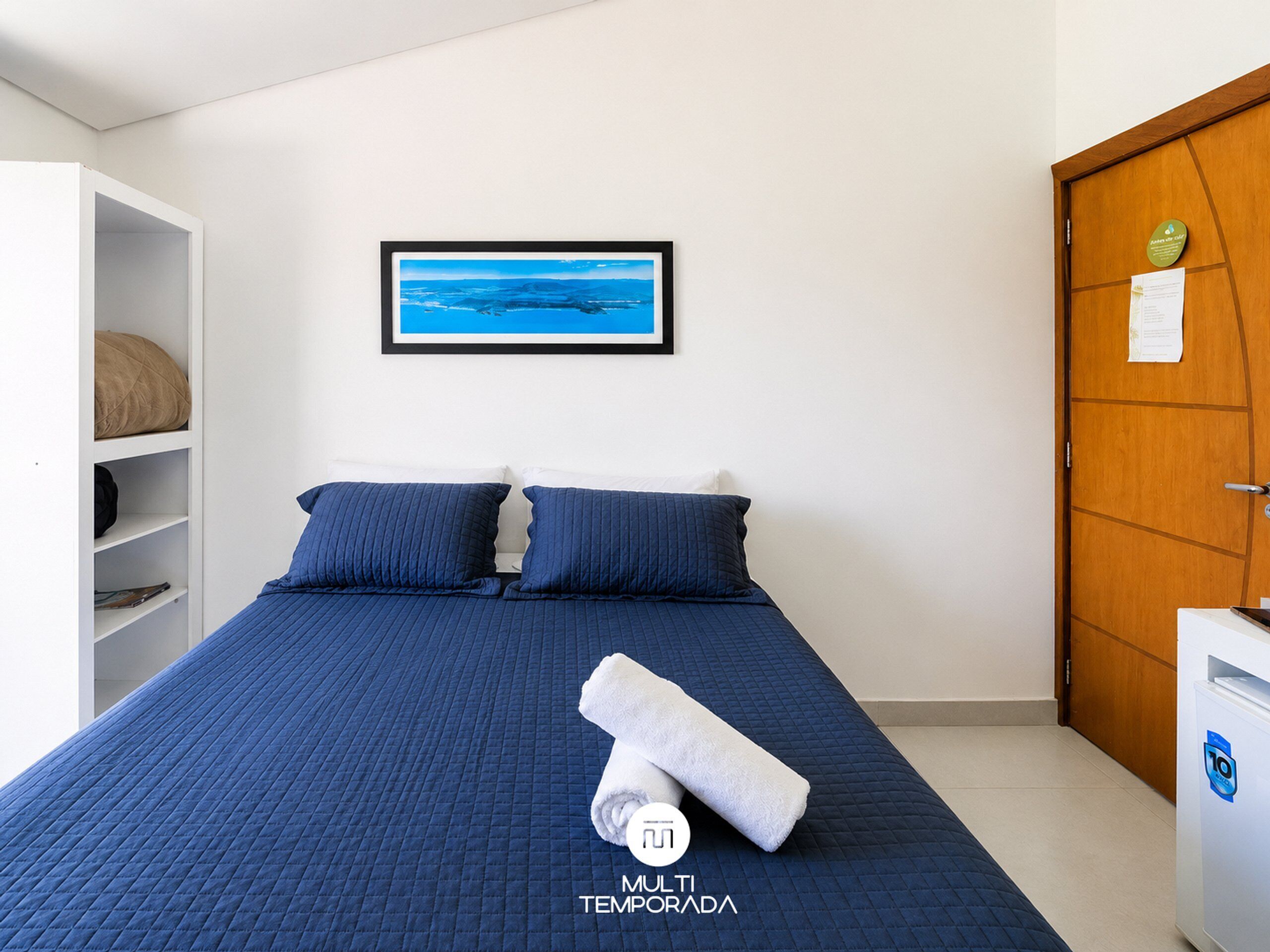 Quarto com cama, almofadas, um quadro na parede, um guarda-roupa e uma porta.
