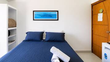 Quarto com cama, almofadas, um quadro na parede, um guarda-roupa e uma porta.