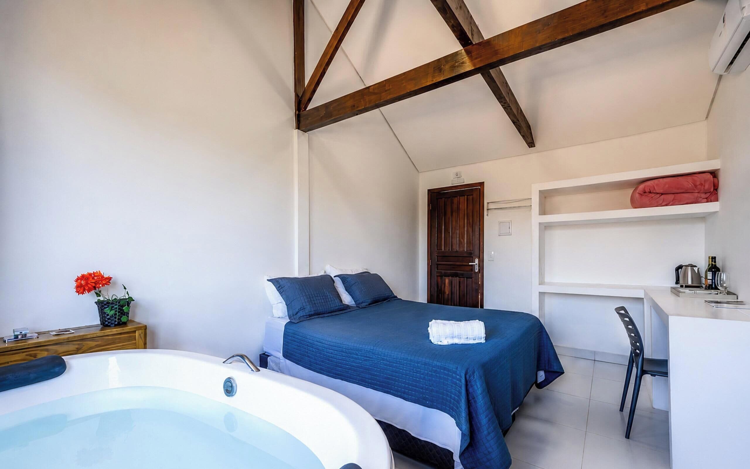 Um quarto com cama, escrivaninha, cadeira, teto de madeira e banheiro com banheira.