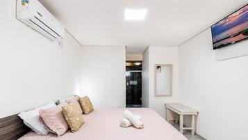Una camera d'albergo con un letto, un comodino, uno specchio, un condizionatore d'aria e una TV a parete.