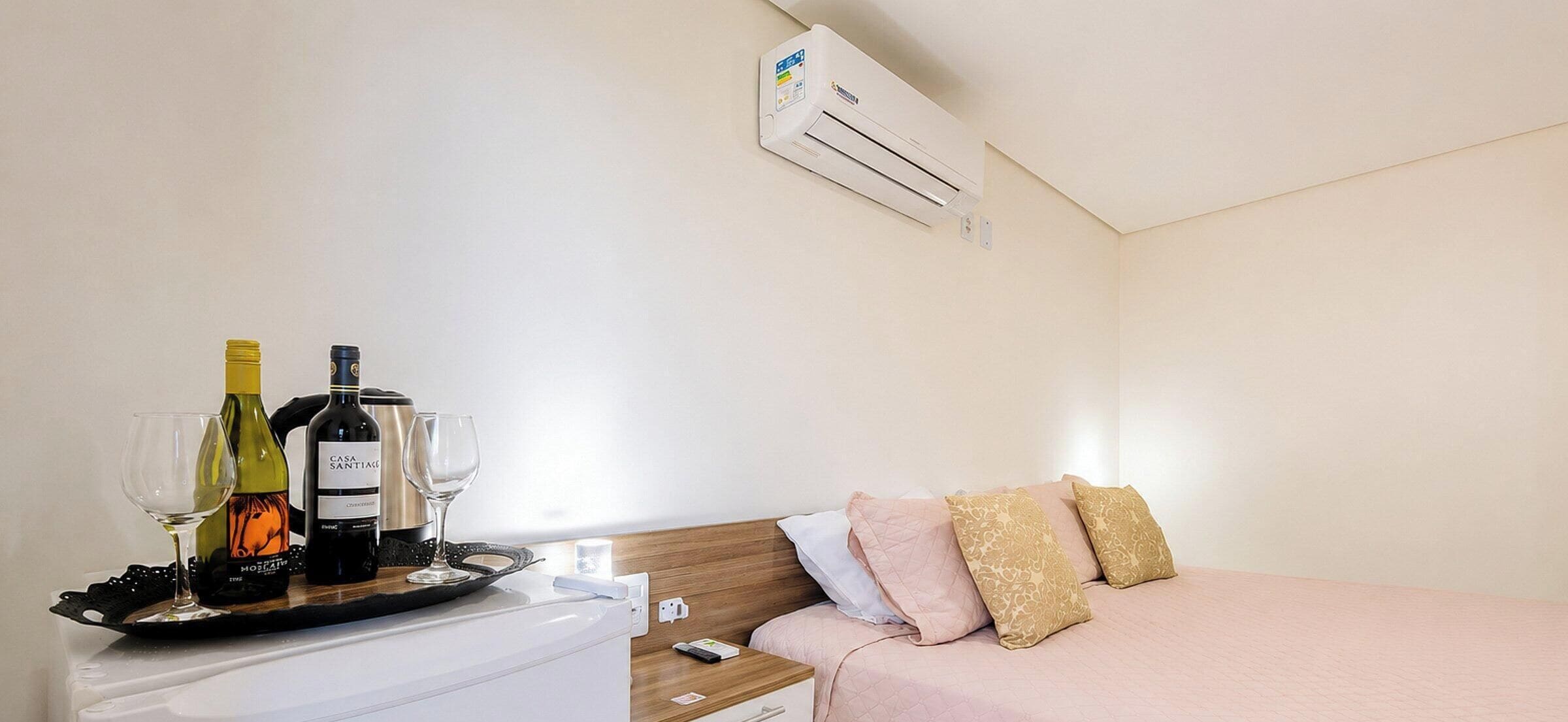 A hotel room with a bed, bedside table, and an air conditioning unit.