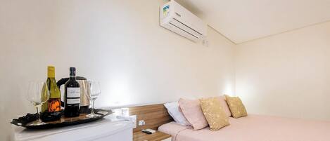 A hotel room with a bed, bedside table, and an air conditioning unit.