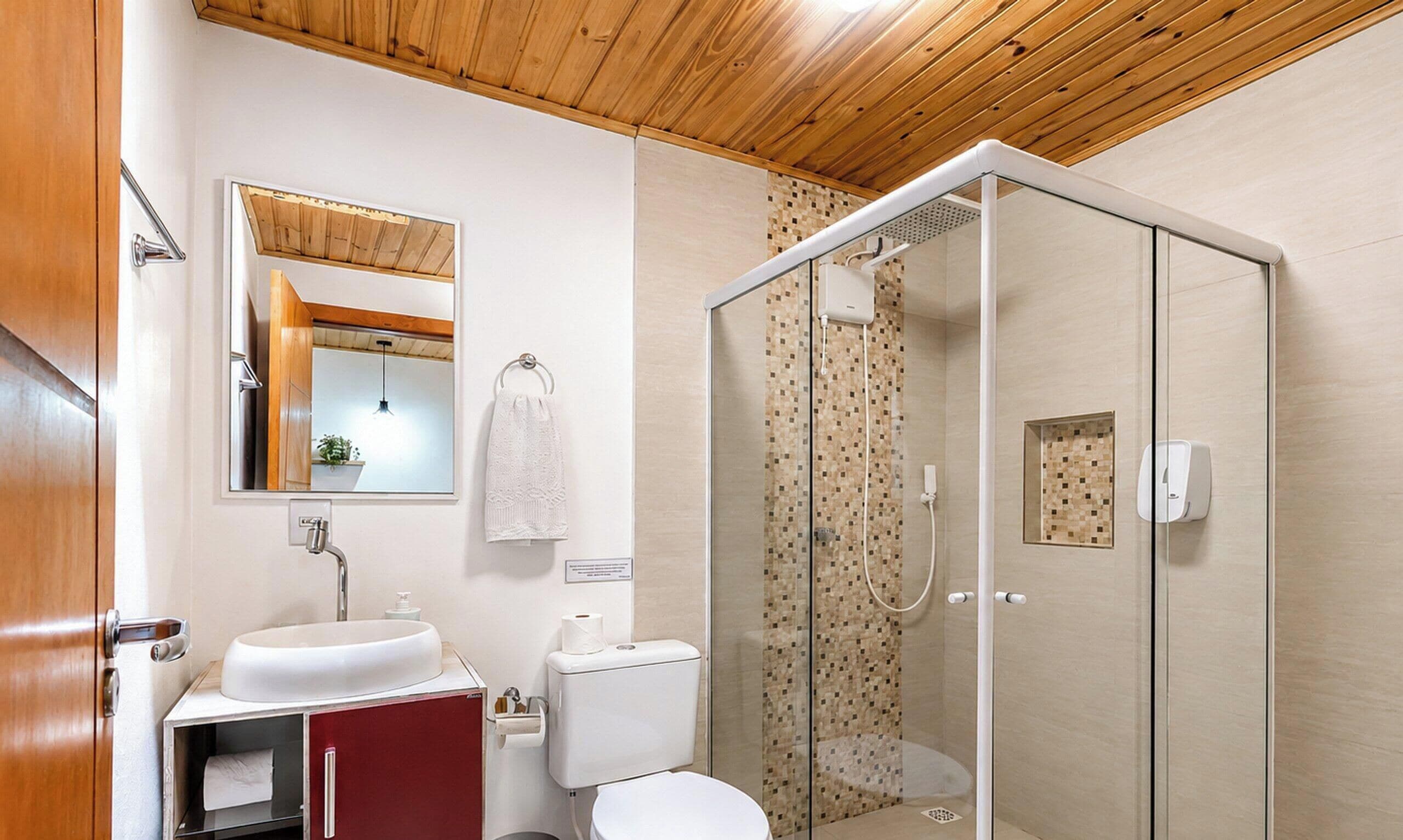 Un baño con techo de madera, cabina de ducha de vidrio, lavamanos blanco y un inodoro.