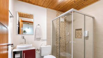 Een badkamer met een houten plafond, een douchecabine van glas, een wit wastafelmeubel en een toilet.