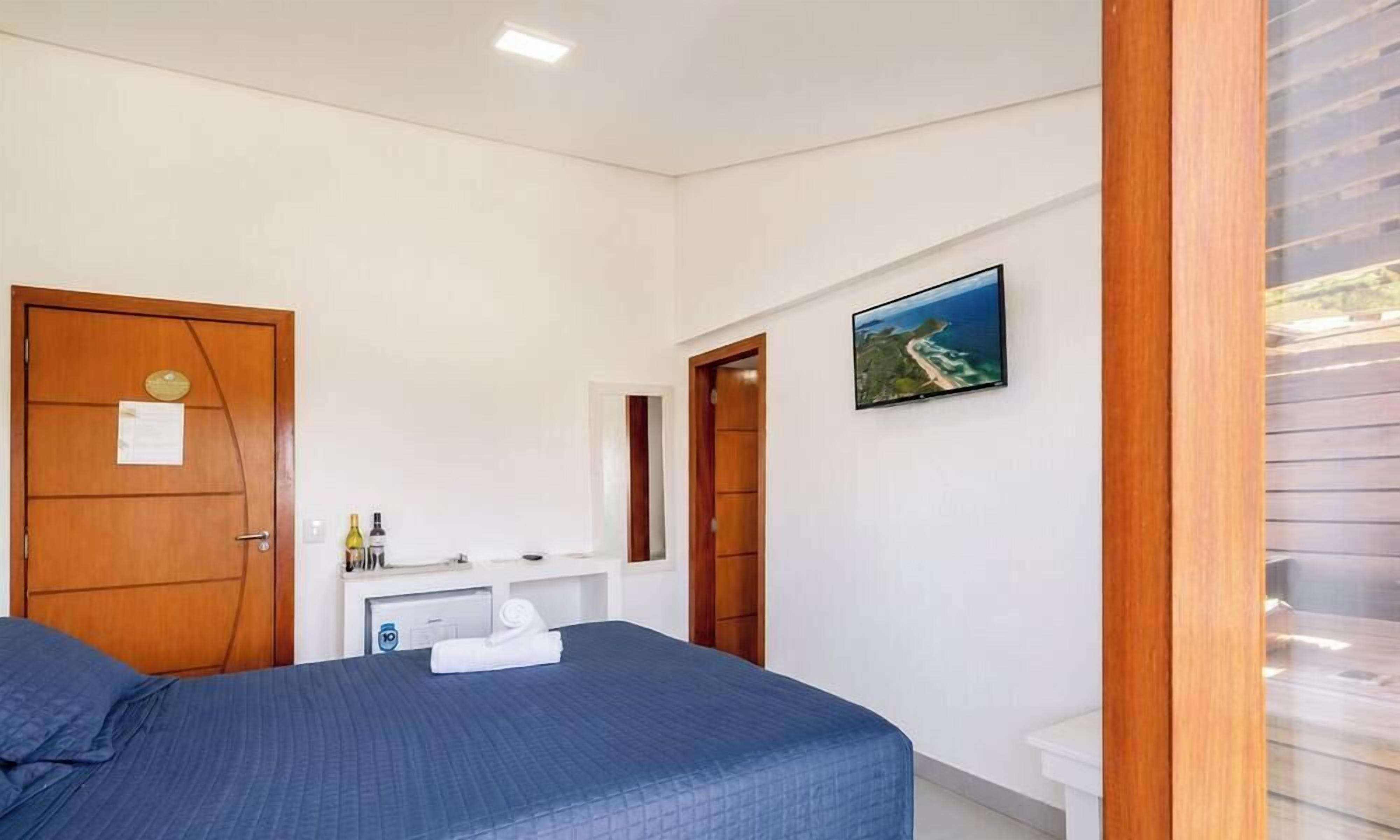 Een slaapkamer met een bed, een houten deur, een klein tafeltje met toiletartikelen, een spiegel en een lijst met een afbeelding aan de muur.