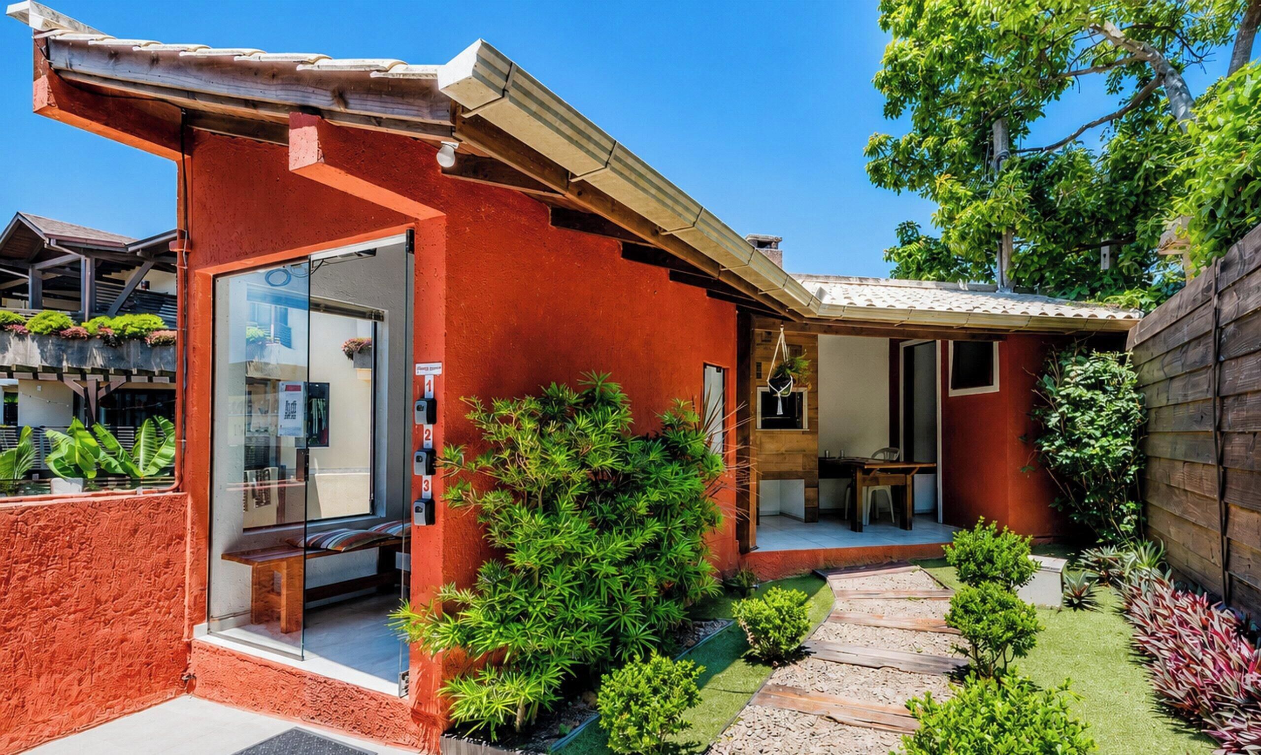 Una casa moderna con fachada roja, puerta de vidrio, pequeño patio y jardín con diversas plantas.