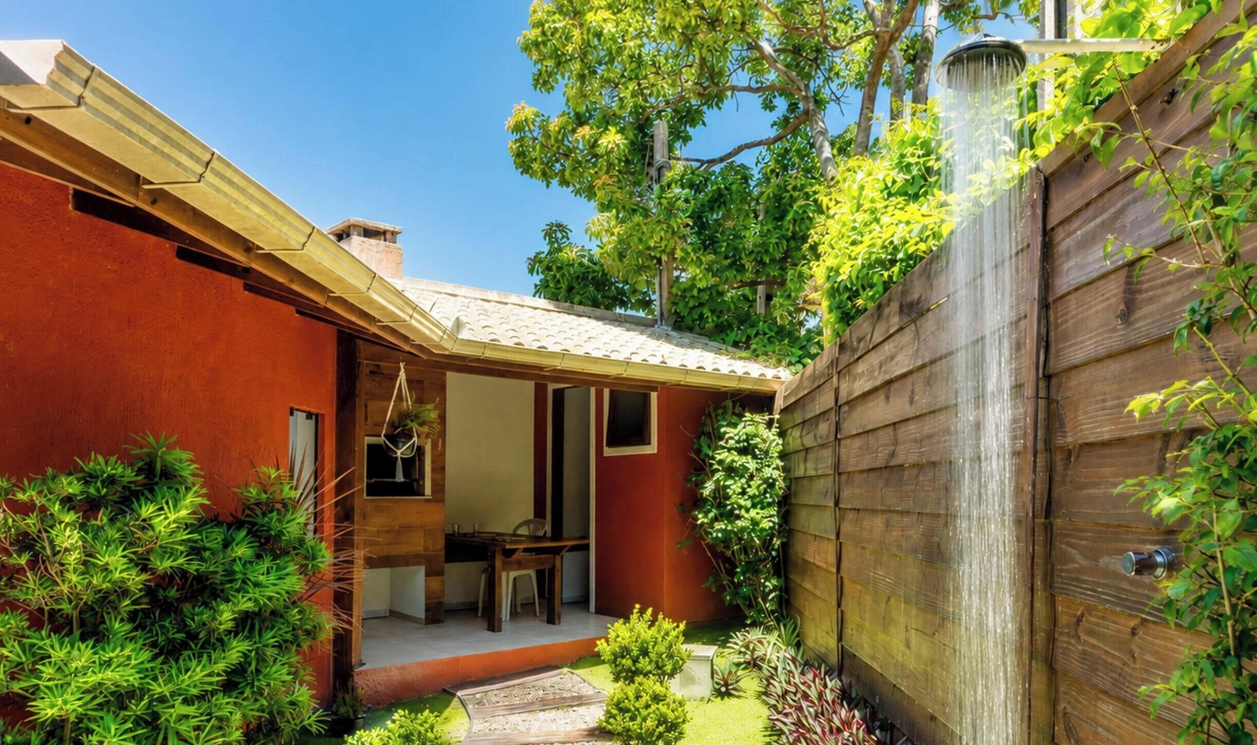 A red building with a covered patio, a wooden fence, and lush greenery.