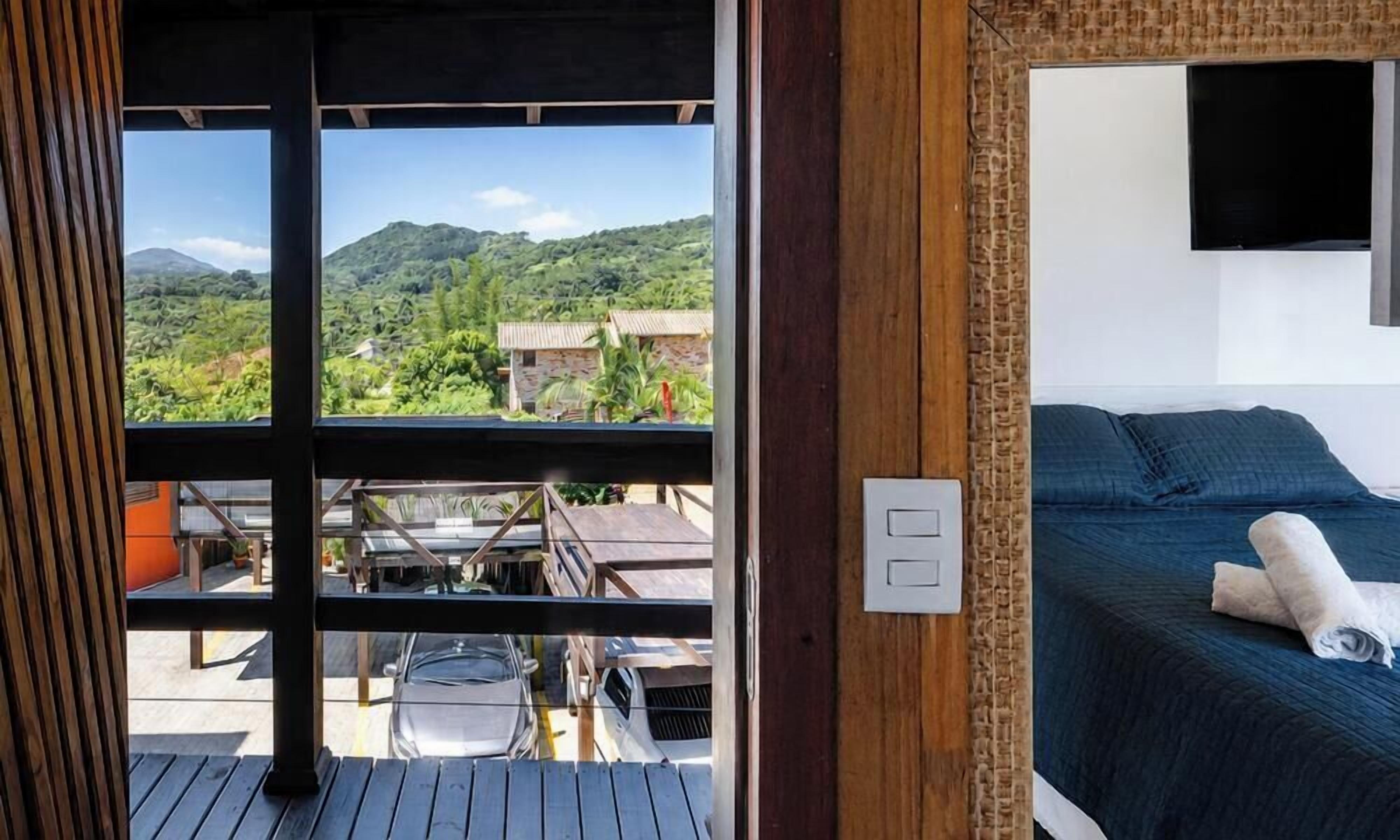 A room with a bed, a TV, and a view of a mountainous landscape through large windows.