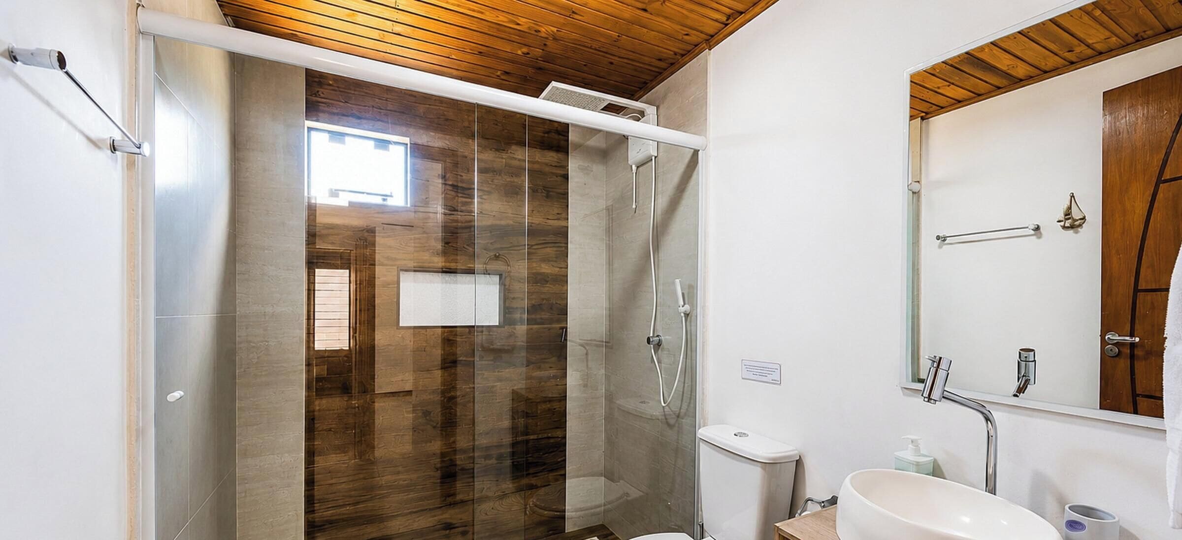 A bathroom with a glass shower enclosure, a wooden ceiling, a white sink, and a wooden door.
