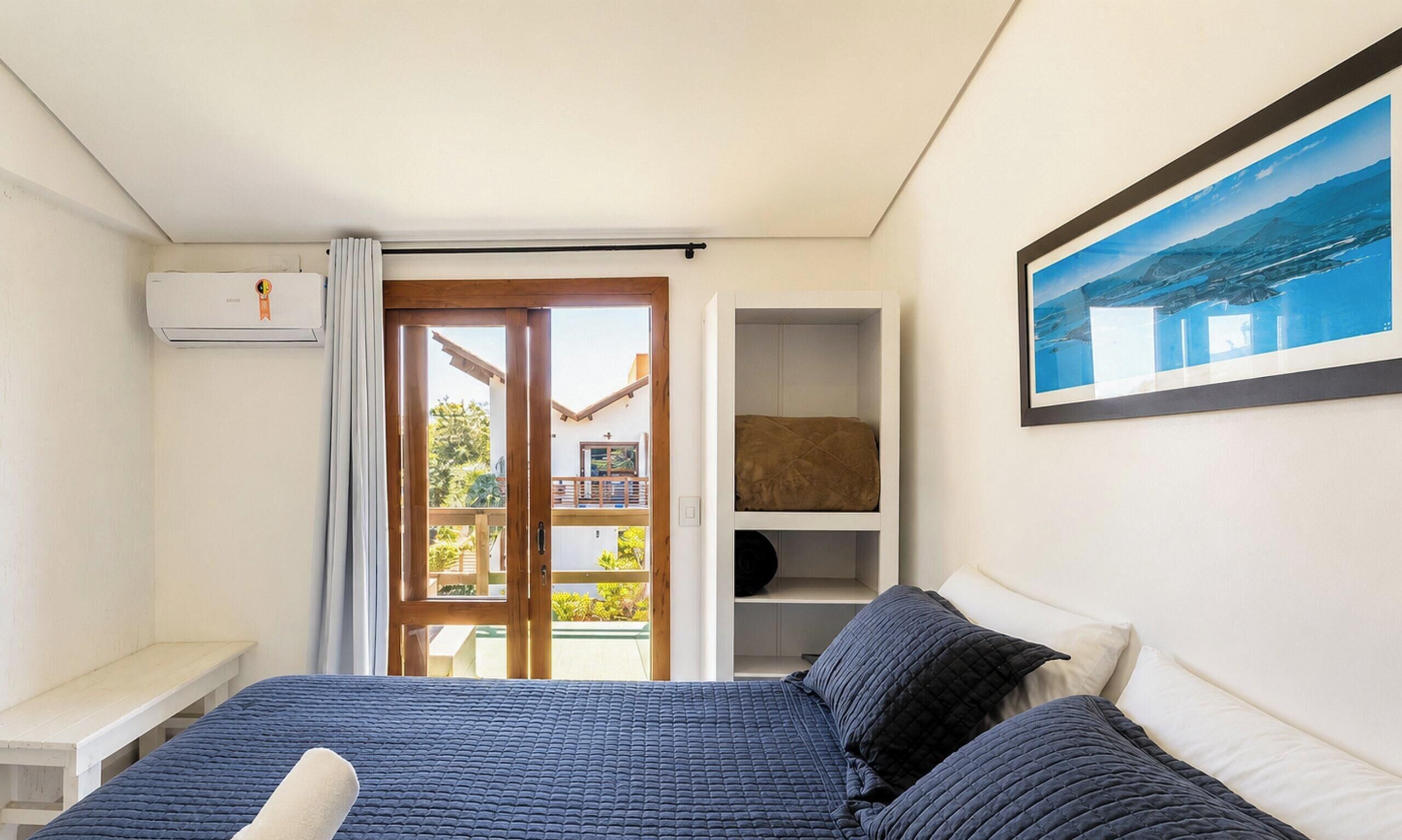 A bedroom with a bed, a window with a view, a shelf, and a painting.