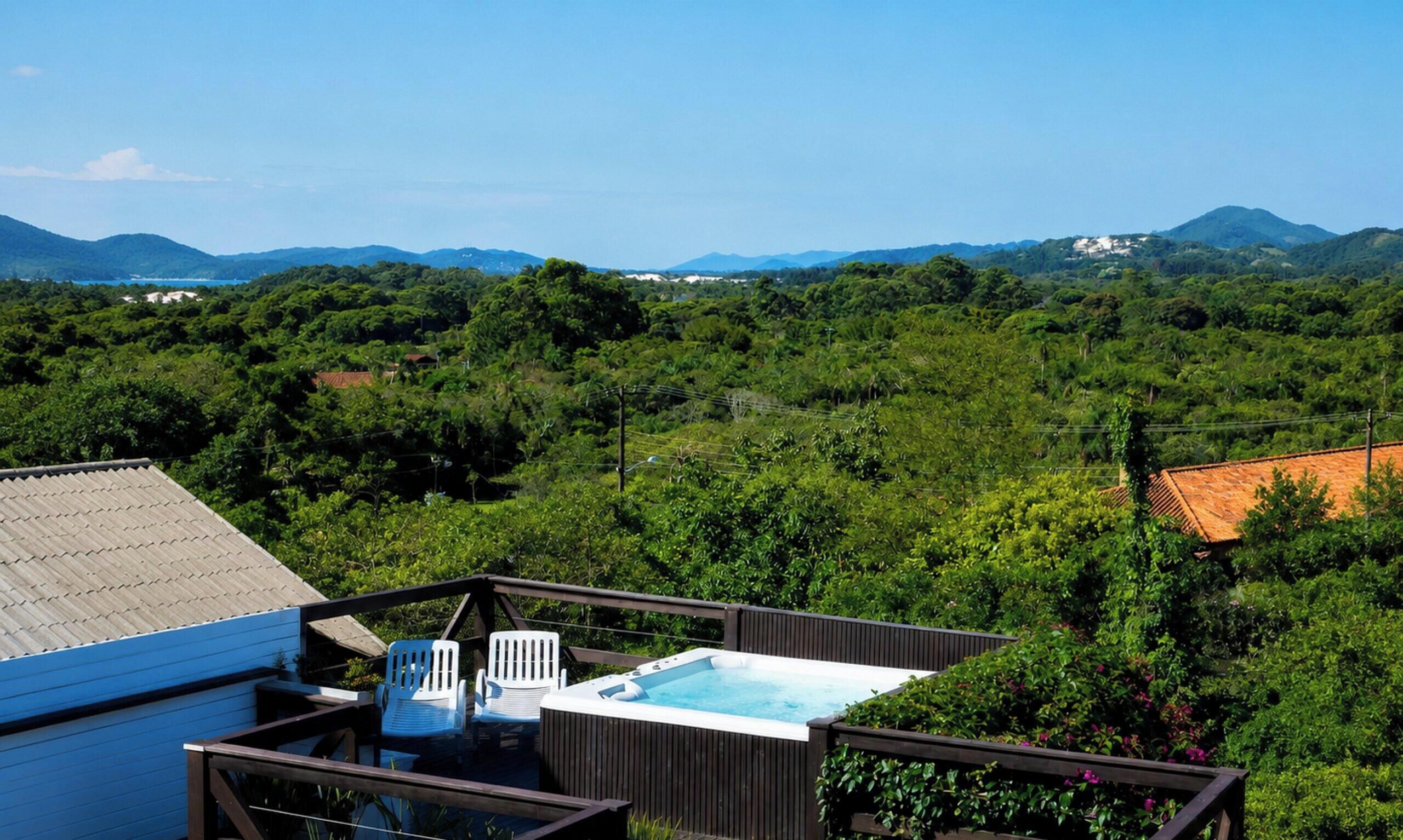 A hot tub on a deck with chairs, surrounded by lush greenery and mountains in the background.