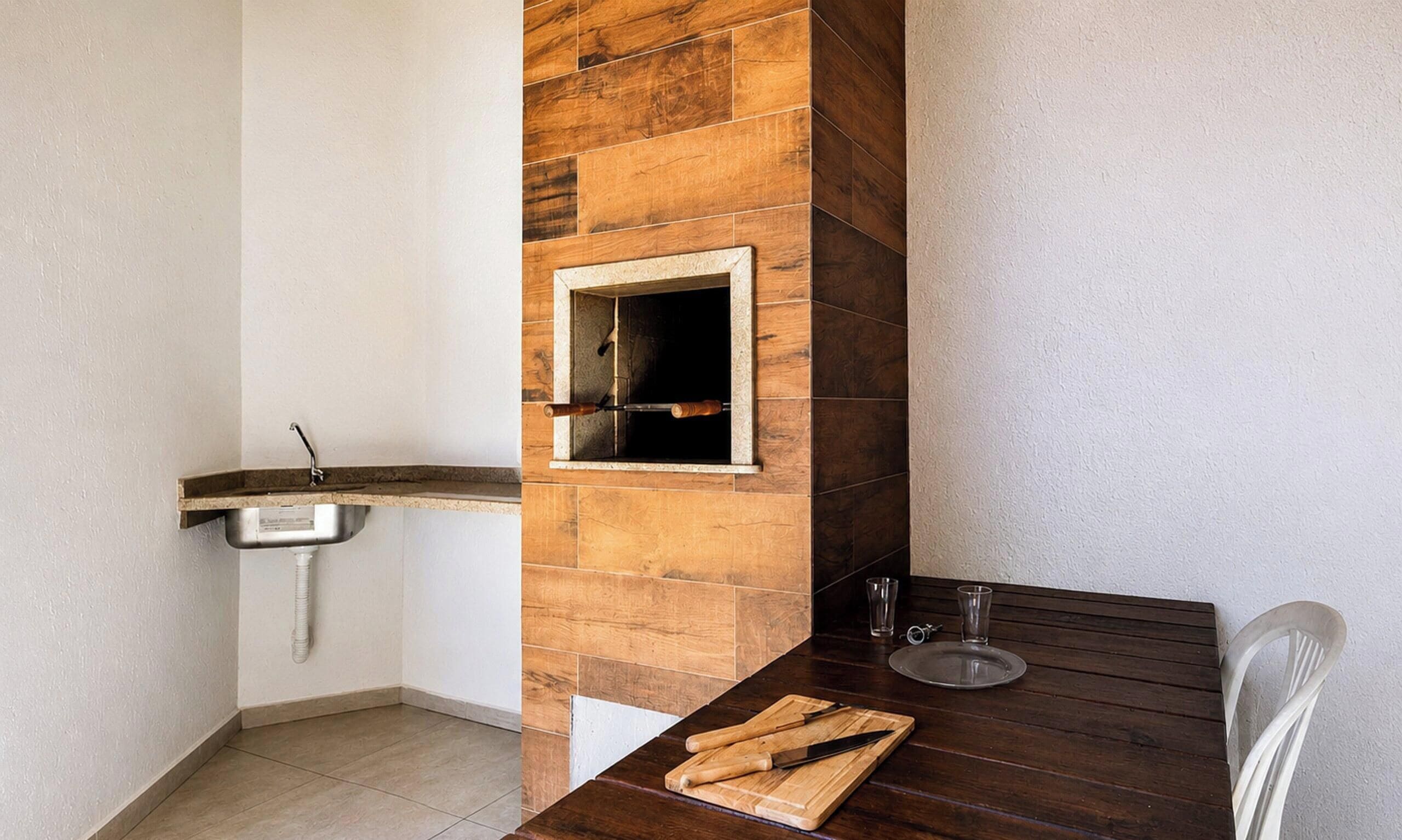 Uma cozinha com painel de parede de madeira, pia e mesa com tábua de corte e utensílios.