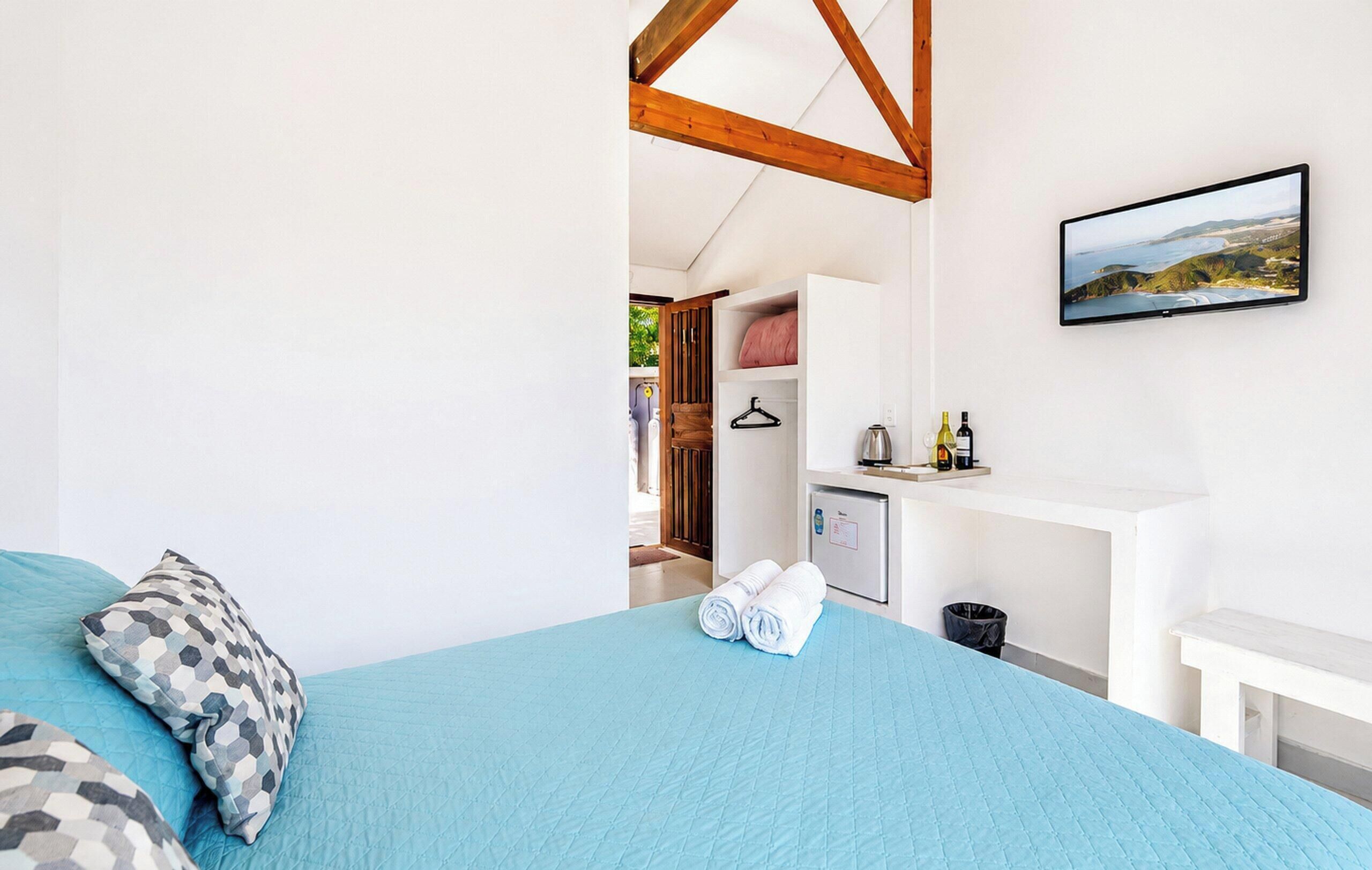 A bedroom with a bed, a hanging TV, a small kitchenette, and a view of the outdoors.