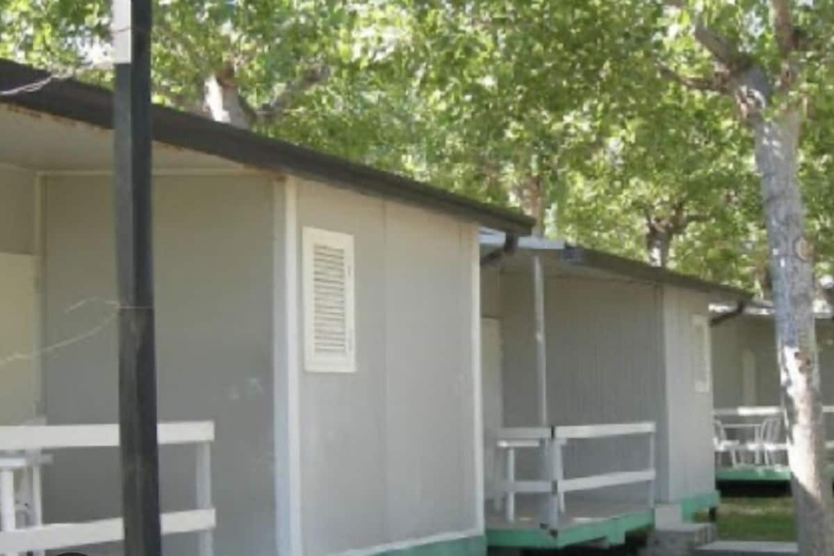 A row of single-story mobile homes with white railings and green steps, surrounded by trees.