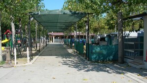 A covered walkway with a playground, trees, and tents. - New Village Europe  (Vasto)