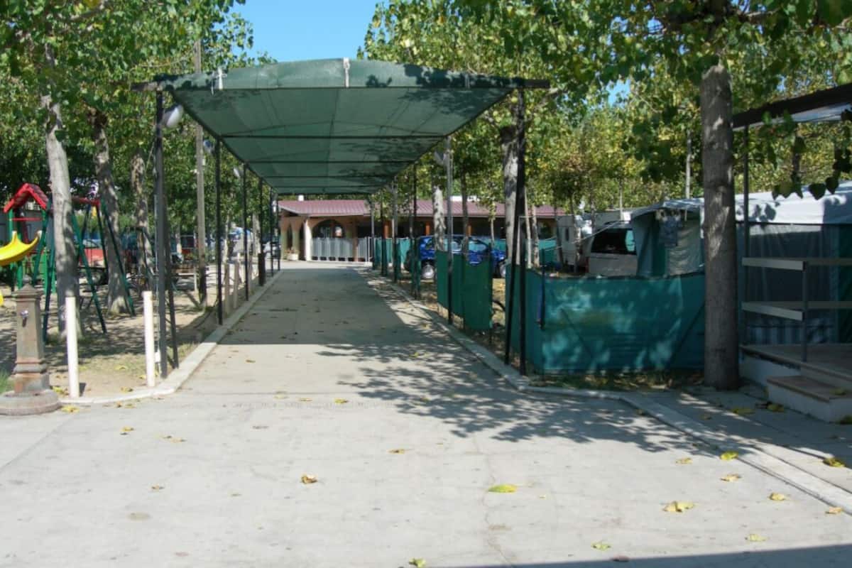 A covered walkway with a playground, trees, and tents.