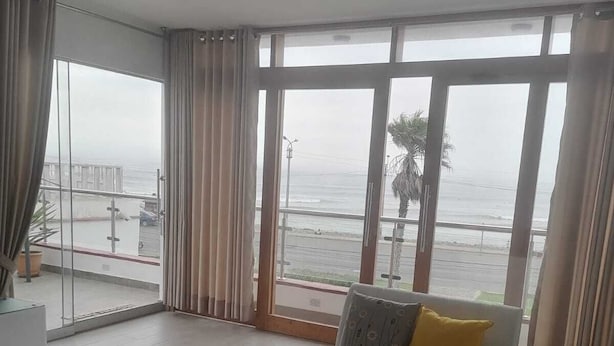 Un salon moderne doté d’une grande fenêtre donnant sur la plage, d’un canapé blanc avec des coussins, d’une table basse en verre et d’un fauteuil blanc.