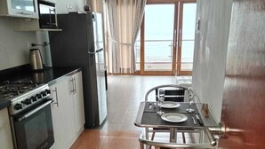 Une cuisine moderne équipée d’une cuisinière, d’un four à micro-ondes et de placards. On y trouve également un coin repas avec une table et des chaises. La pièce est dotée d’une grande fenêtre avec des rideaux, offrant une vue sur l’extérieur.