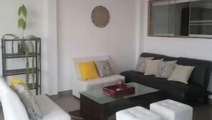 Un salon moderne avec un canapé blanc, un canapé noir, une table basse en verre et une petite table d’appoint blanche.
