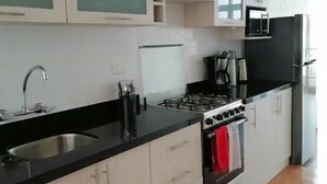 Une cuisine moderne avec des meubles blancs, un plan de travail noir, un évier en acier inoxydable, une cuisinière à gaz et un réfrigérateur noir.
