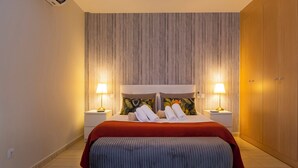 Siististi järjestetty hotellihuone, jossa on sänky, kaksi yöpöytävalaisinta, penkki ja vaatekaappi.