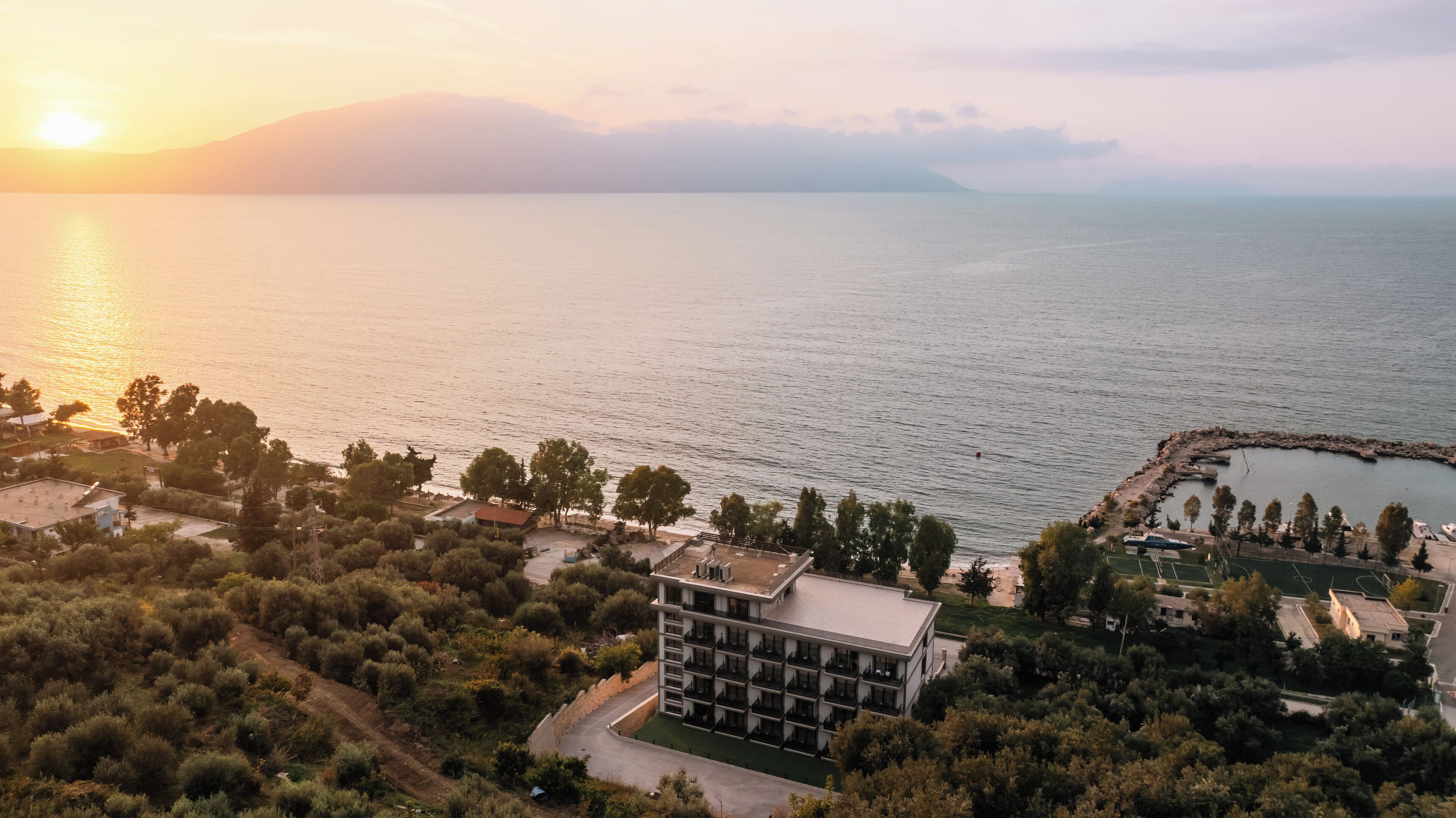 Ein Küstenhotel im modernen Stil, mit einem zentralen Gebäude und zahlreichen Balkonen, umgeben von üppiger Vegetation und Blick auf das Meer.