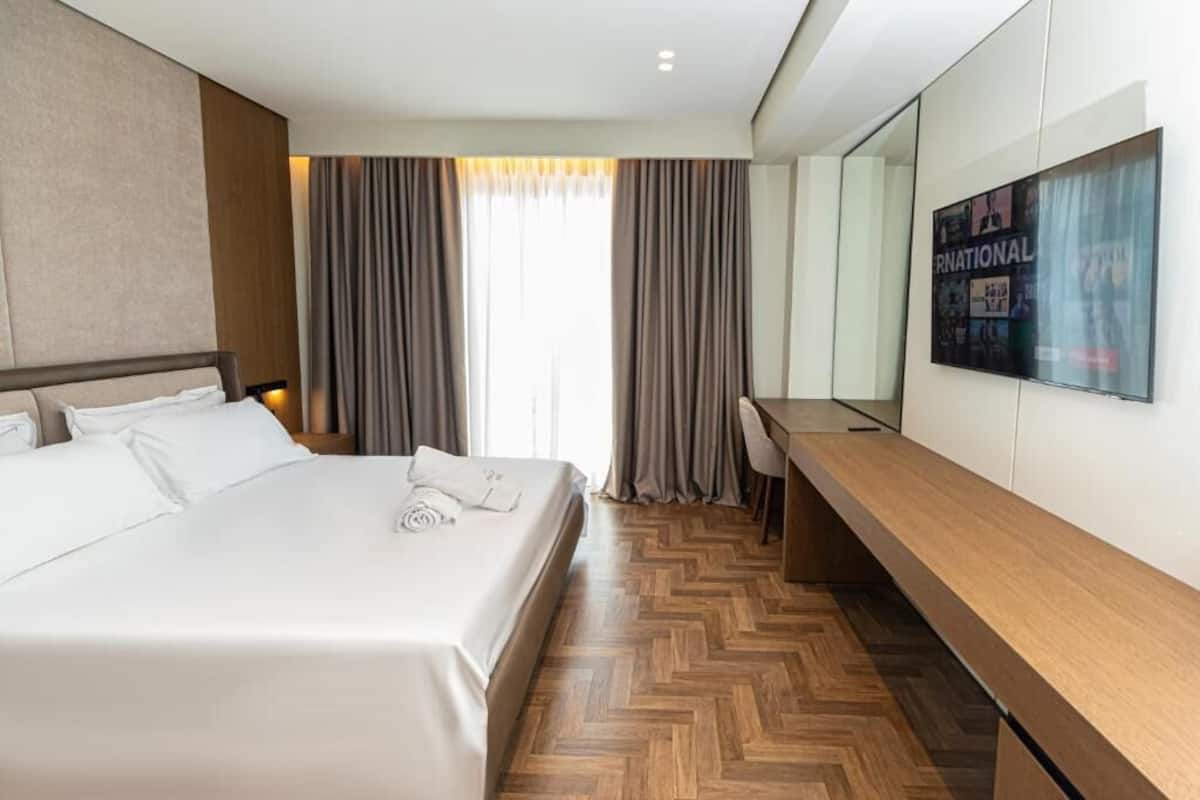 Een hotelkamer met een groot bed, een houten bureau, een televisie en een spiegel.