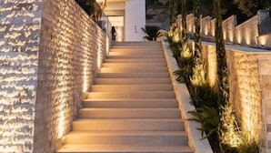 Un bâtiment moderne doté d’un escalier menant à un balcon, entouré de murs en pierre et de verdure.