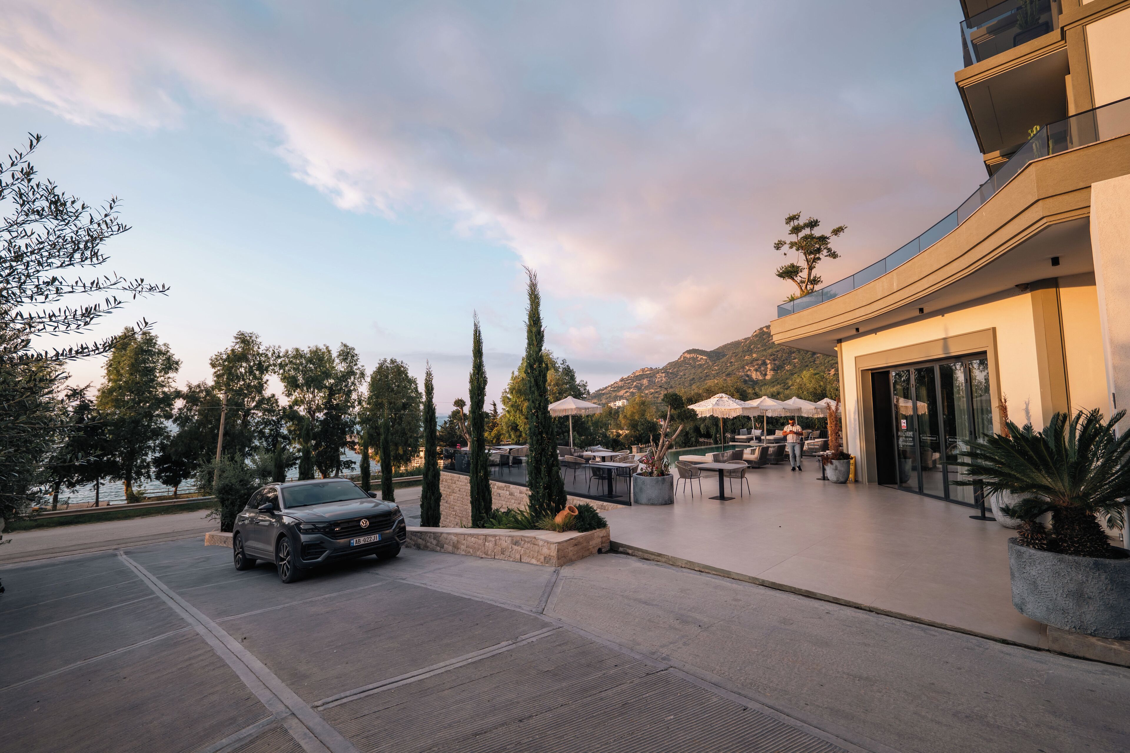 Un hotel moderno con terraza, zona de estacionamiento y vistas a la montaña.