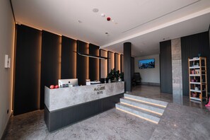 A hotel reception area with a marble counter, a television, and a staircase leading to the upper floor.