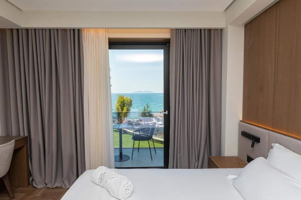 Een hotelkamer met een bed, een bureau en uitzicht op de zee door een glazen deur.