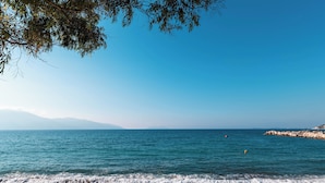 Une plage à l’eau d’un bleu limpide, bordée de galets, avec des montagnes qui se dessinent à l’horizon.
