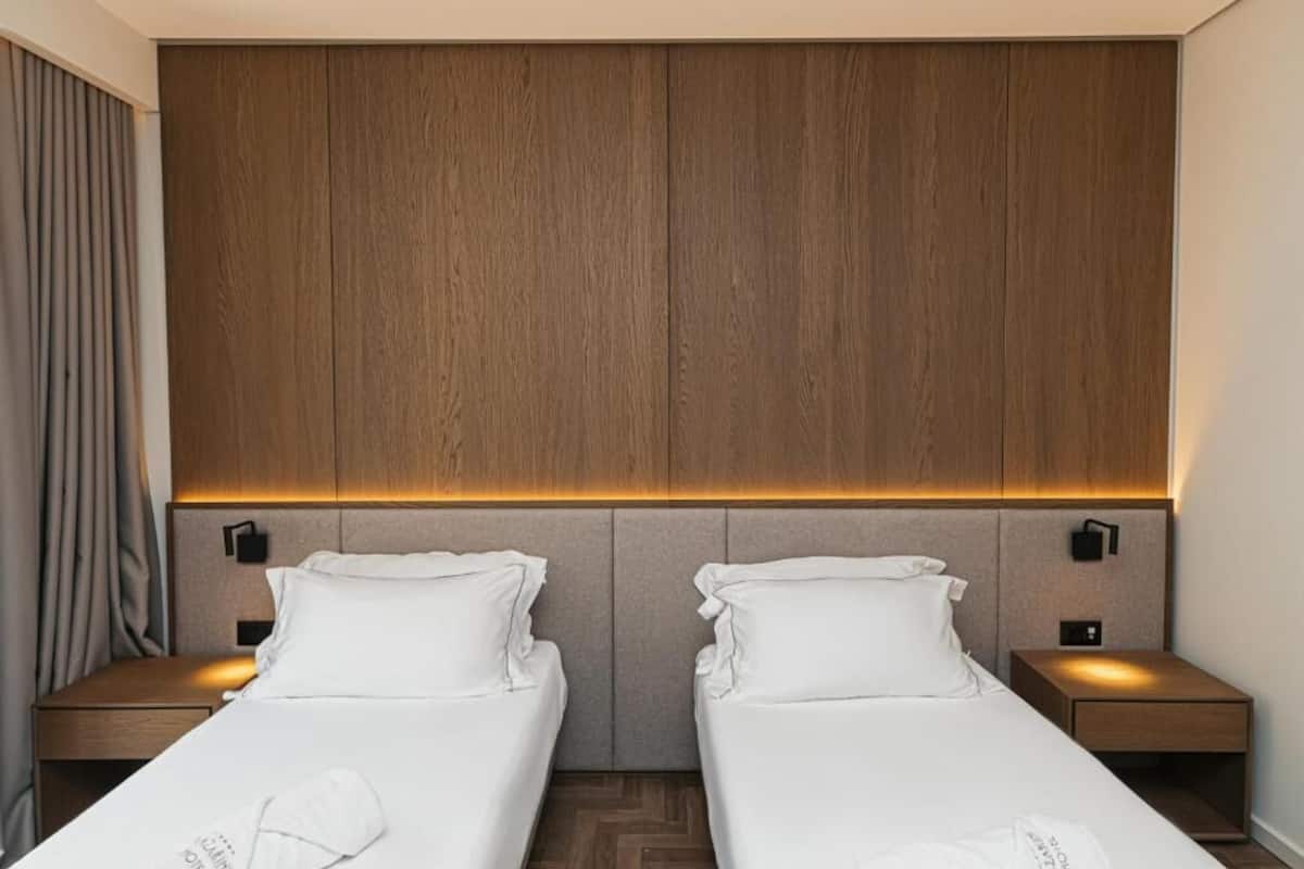 Een hotelkamer met twee eenpersoonsbedden, een houten hoofdbord, bedlampjes en een nachtkastje met een lamp.