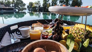 Desayuno con huevos, frutas y bebidas junto a una piscina.