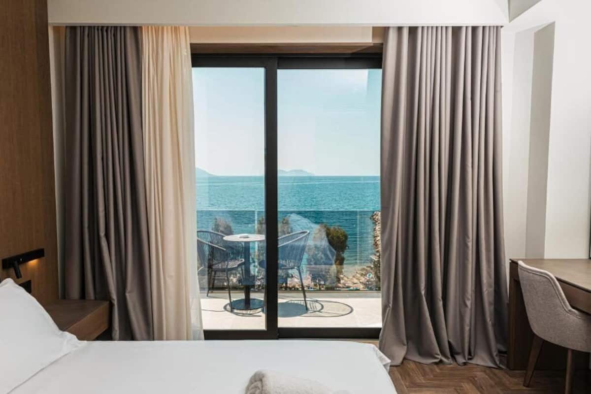 Een hotelkamer met een bed, een bureau en uitzicht op de zee door een glazen deur.