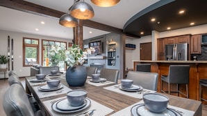A modern dining area with a long wooden table set for six, surrounded by leather chairs.