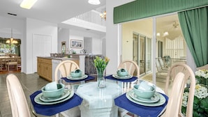 Un coin repas avec une table en verre dressée pour quatre personnes, entourée de chaises sur lesquelles sont posés des sets de table bleus.
