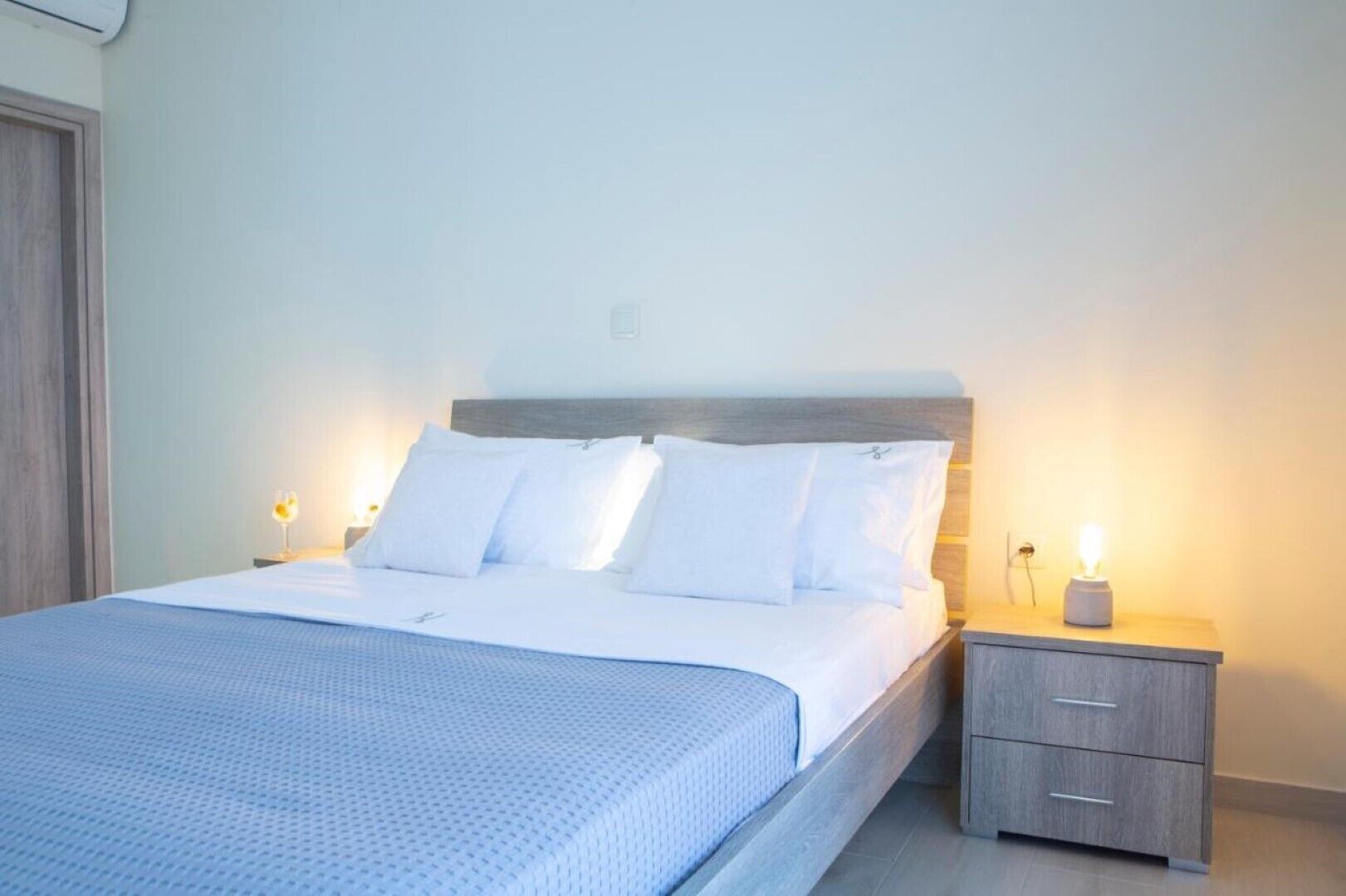 A neatly made bed with white linens and pillows, a wooden headboard, and two bedside tables with lamps.
