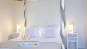 Una habitación de hotel con una cama, dos mesitas de noche con lámparas, una bandeja con vasos y una botella, y una cama con dosel.