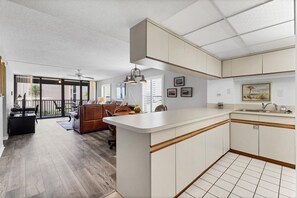 Una cocina amplia con una isla grande, armarios blancos y vistas a un balcón.